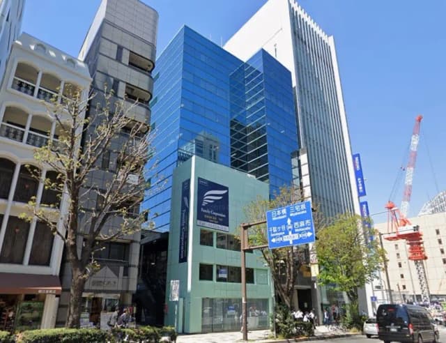 青いガラスのファサードを持つ現代的なオフィスビルと周囲の街並み、晴天のもとでの都市の風景
