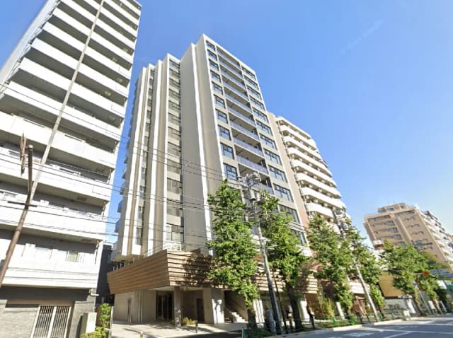 - モダンなマンションの外観、周囲に緑の樹木があり、青空の下で映える景観