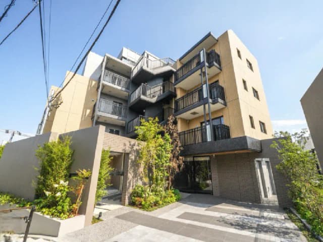 - モダンな外観の集合住宅、バルコニー付きで緑豊かなエントランス、周囲に自然光が差し込む明るい雰囲気