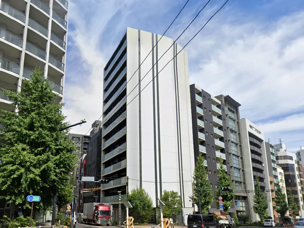 - 都市部に立地する複数の高層マンション、青空と雲を背景にした現代的な建物群、道路脇の緑豊かな木々