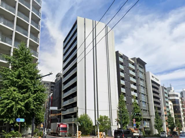 - 都市部に立地する複数の高層マンション、青空と雲を背景にした現代的な建物群、道路脇の緑豊かな木々