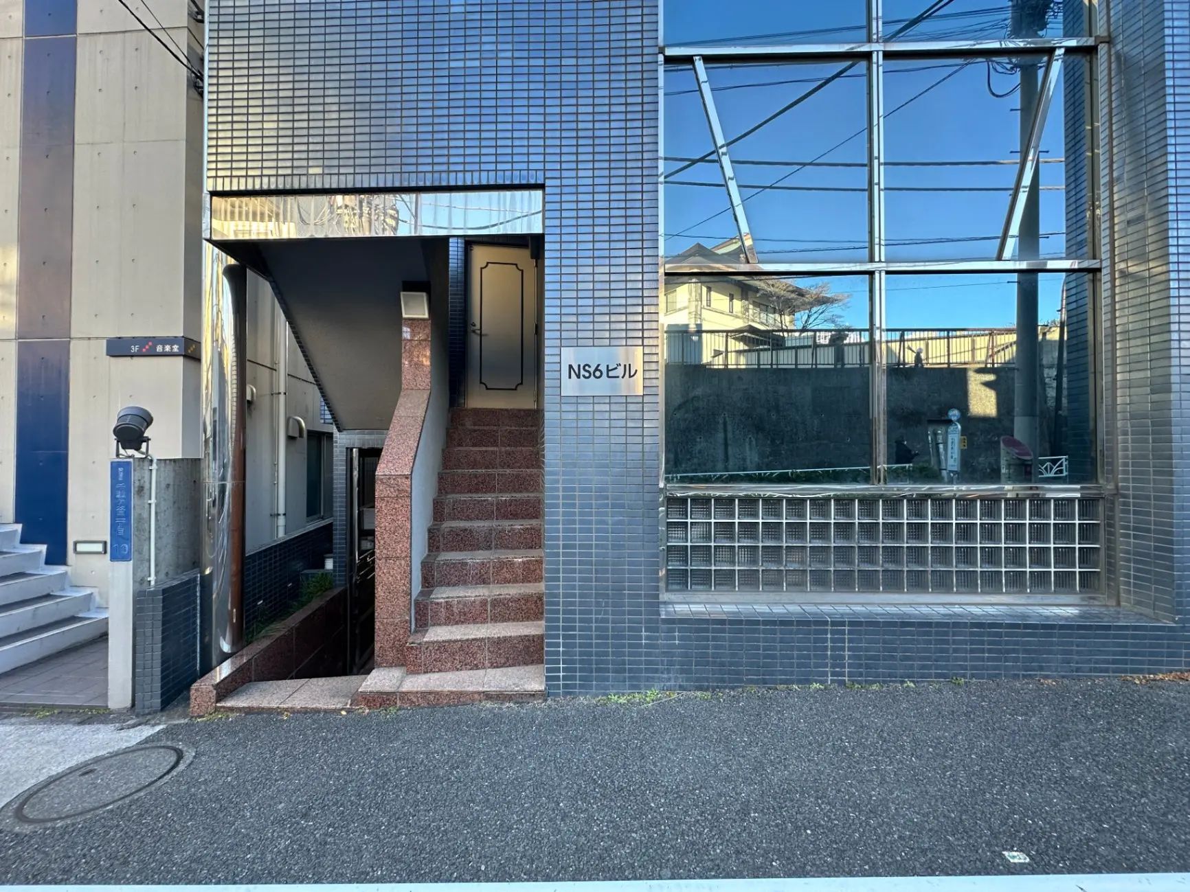 都会の景観に溶け込む現代的なビルのエントランス、大きなガラス窓とモザイクタイルの外観デザイン