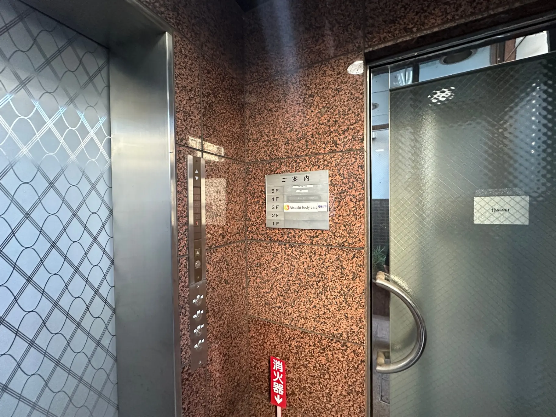 ビルのエレベーター内部、ボタンパネルの隣に案内看板が設置されたインテリア