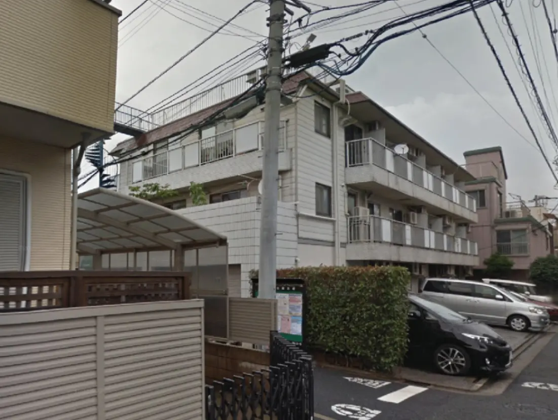 - 複数のアパートメントビルが並ぶ住宅街の風景、駐車場と緑の生垣が見える外観