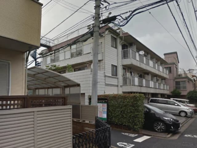 - 複数のアパートメントビルが並ぶ住宅街の風景、駐車場と緑の生垣が見える外観