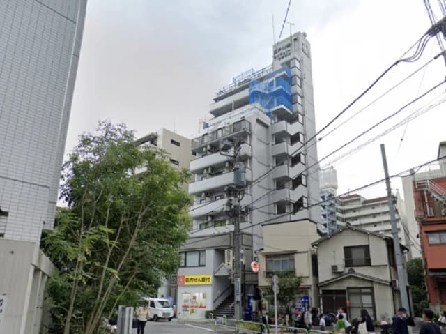 - 都市の風景に立つ高層マンション、周囲に住宅街と緑の木々、電柱が混在する街並みの情景