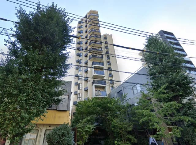 - 高層マンションの外観、周囲に生い茂る木々と電線が見える都市風景