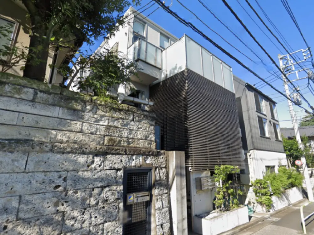 - モダンな外観の住宅、黒い木目調のパネルとガラスを使用し、緑豊かな植栽が施されたエントランスの風景