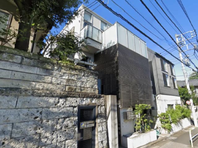 - モダンな外観の住宅、黒い木目調のパネルとガラスを使用し、緑豊かな植栽が施されたエントランスの風景
