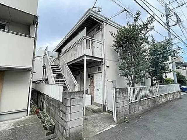 - アパートの外観、2階建ての建物、階段が見えるエントランス、周囲に緑や電線がある住宅地の景観