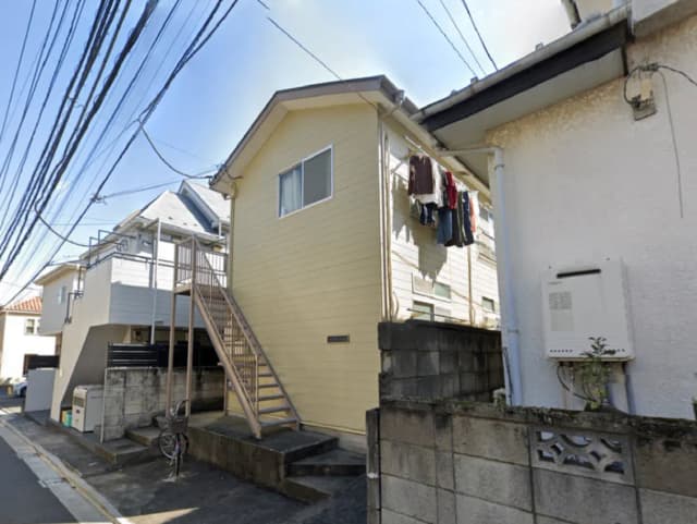 - 脇道に面した2階建ての住宅、洗濯物が干されたバルコニー、階段と近隣の電線が見える風景