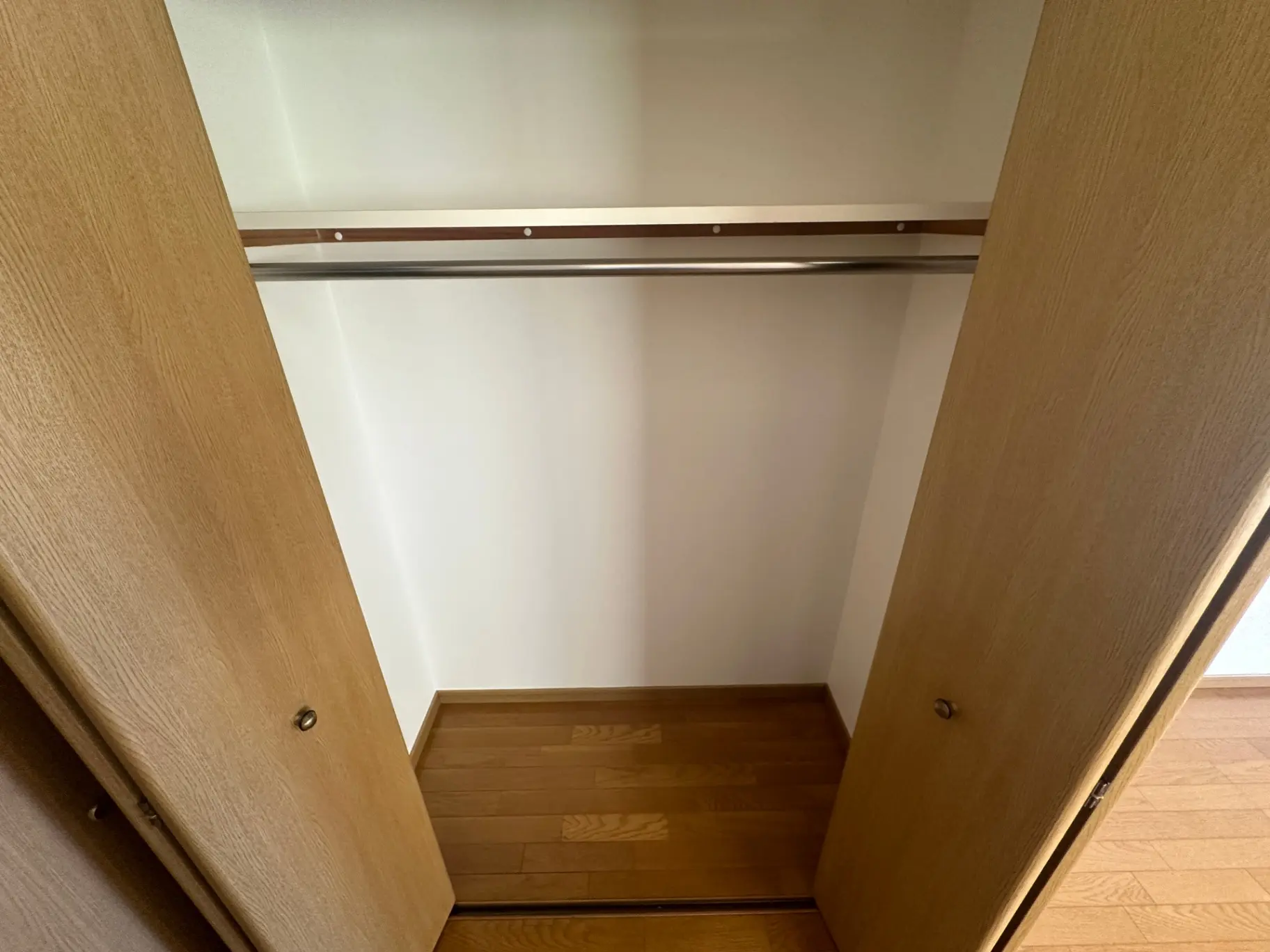 木製のドアと木目調のフローリングが特徴的な空のクローゼット、明るい室内空間