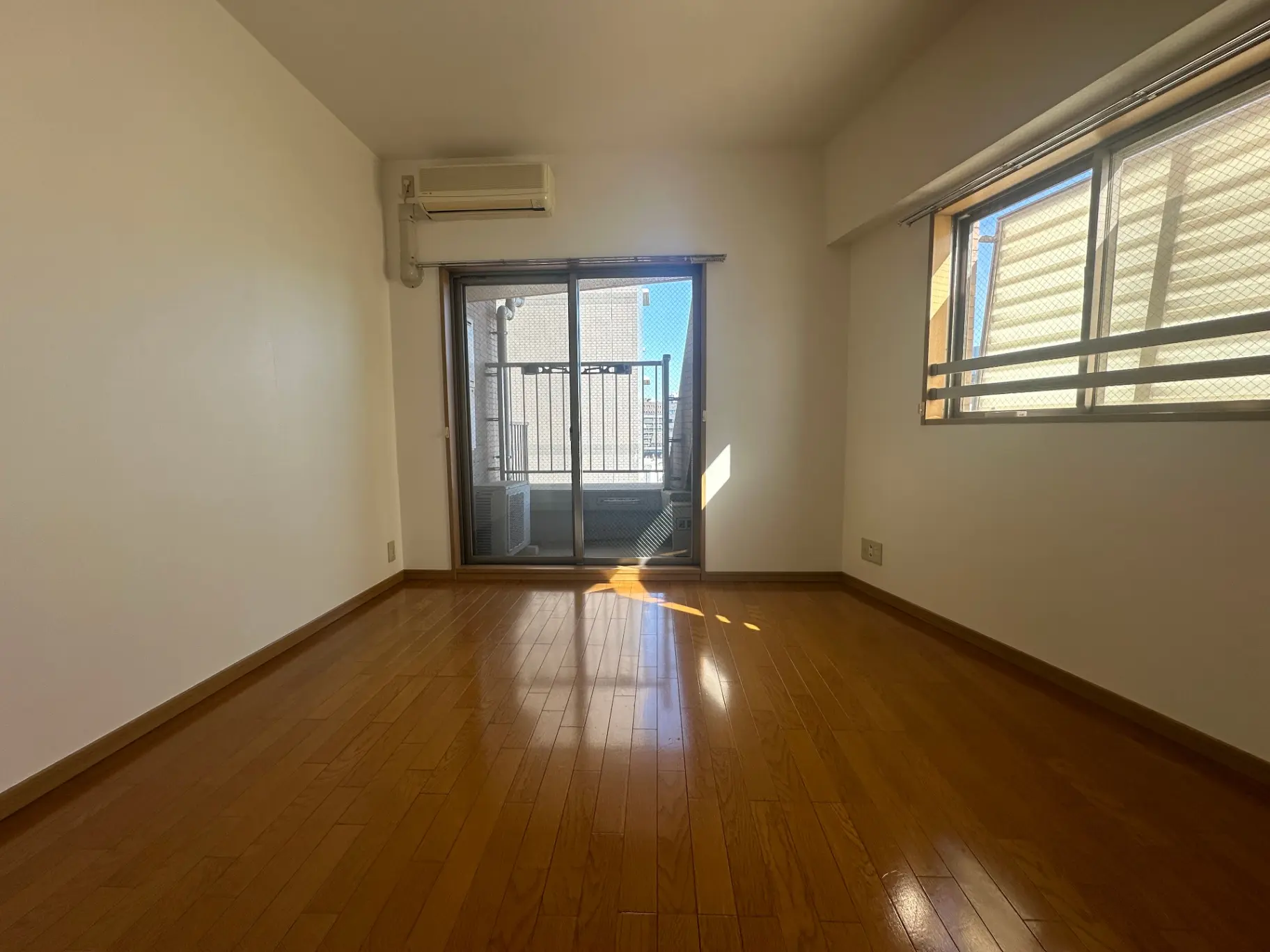 明るい日差しが差し込む空の部屋、木製フローリングとベランダ付きのリビングルーム