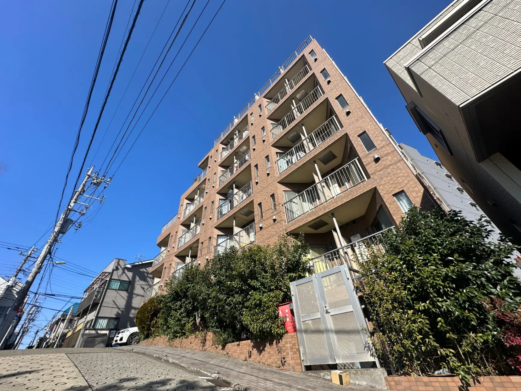 日当たりの良い都市型マンション、青空と緑豊かな植栽が映える外観