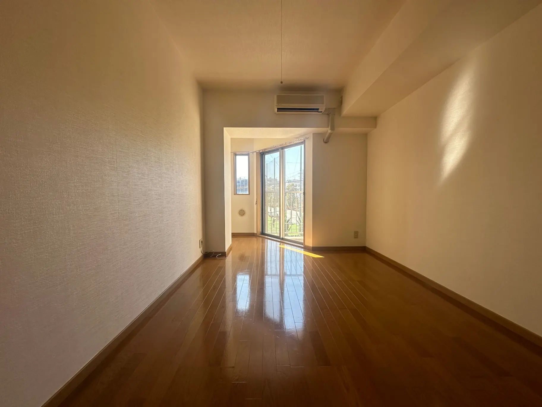 明るい日差しが差し込む広々とした空の部屋、ベランダ付き、木製フローリングのインテリア