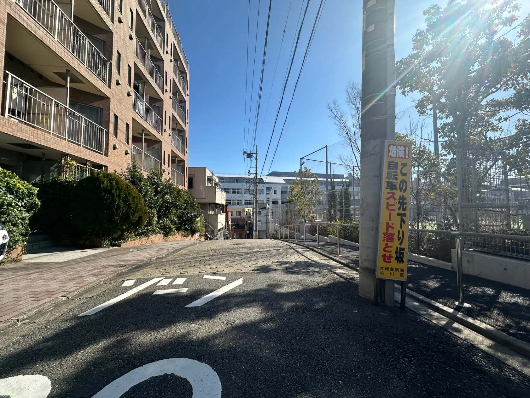晴れた日の住宅街、アスファルトの道路とマンション、公園の緑と「高齢者と子供に優しいまち」の看板