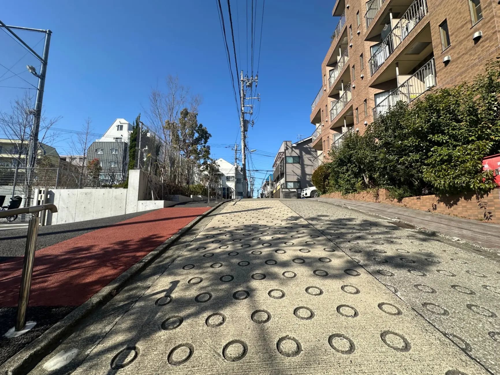 晴れた日の都市の住宅街の道路、歩道には点字ブロックがあり、マンションと一軒家が並ぶ景観
