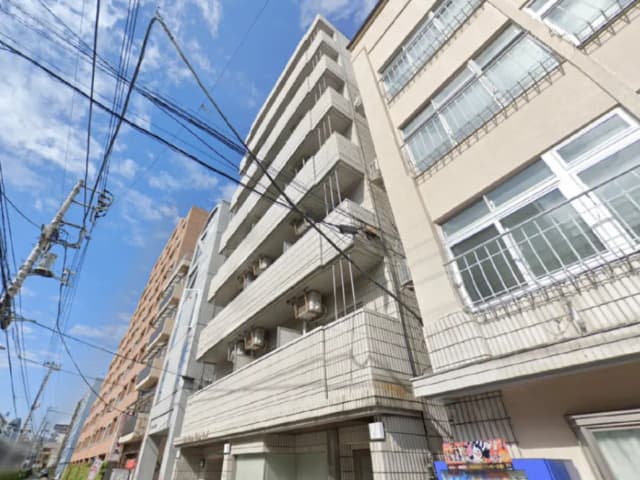- 狭い路地に建つグレーの外壁を持つ中規模アパートメントと青空、電線が横断する街の風景