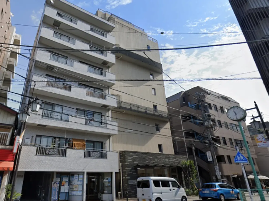 - 都市部に建つモダンなマンション、白い外壁とバルコニーを持ち、周囲には他の建物と街の景色が広がる風景