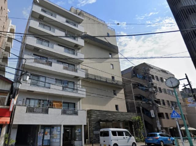 - 都市部に建つモダンなマンション、白い外壁とバルコニーを持ち、周囲には他の建物と街の景色が広がる風景