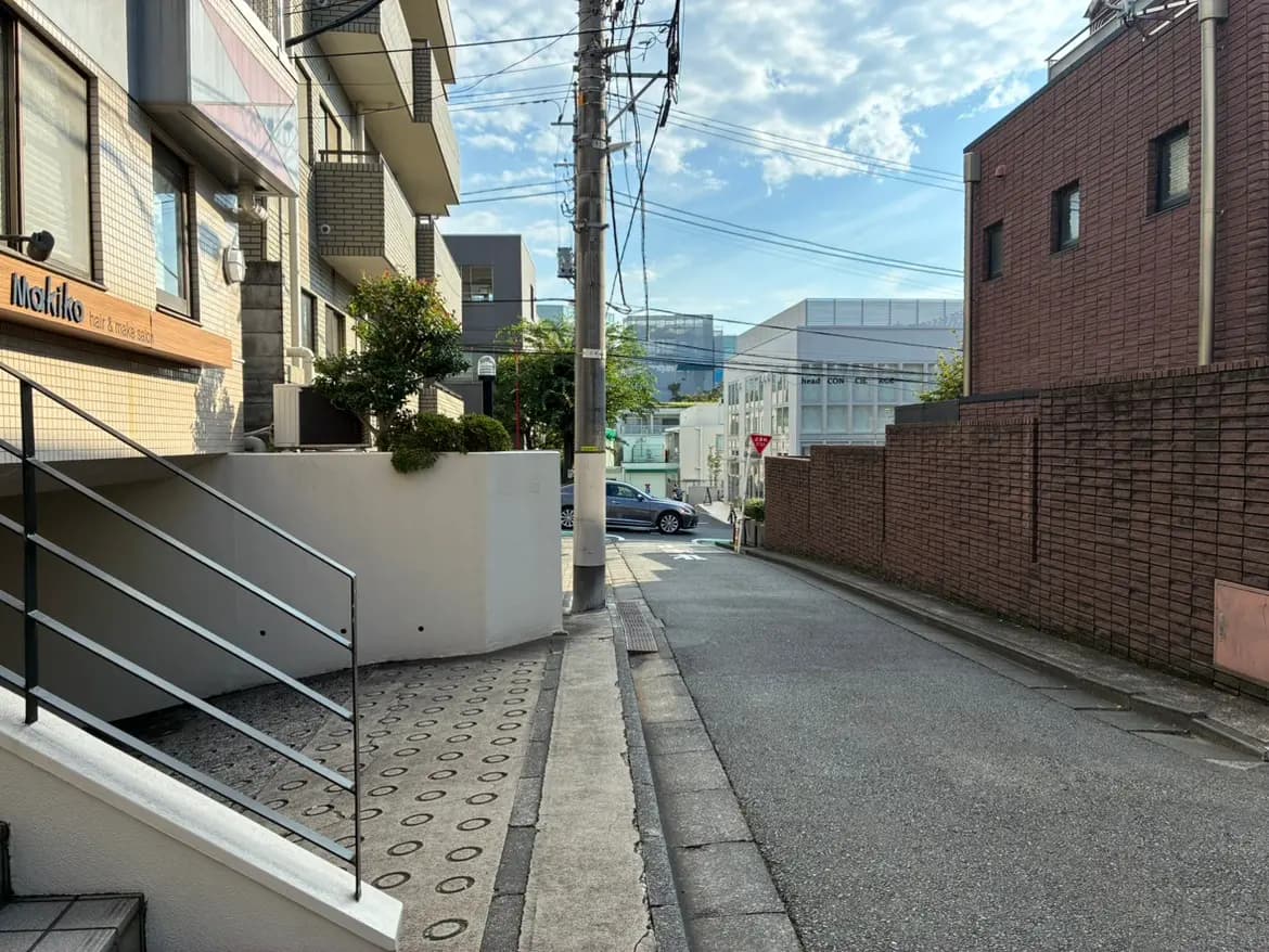 - 髪型サロン「Mokito」の入口と周辺の住宅街、階段と舗装された道路がある静かな風景