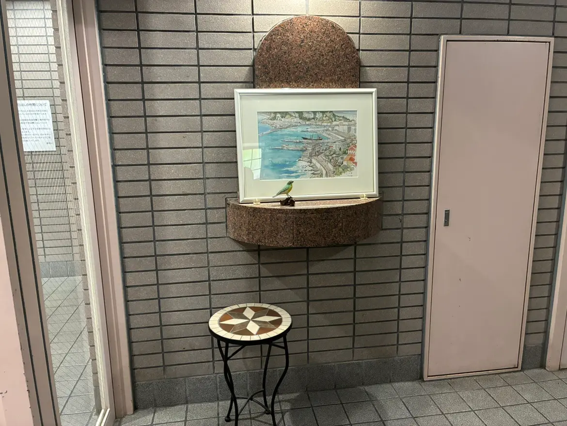 - グレーのタイル壁に囲まれたエントランスのスペース、アート作品と小さなテーブルが置かれたシンプルでスタイリッシュなインテリア