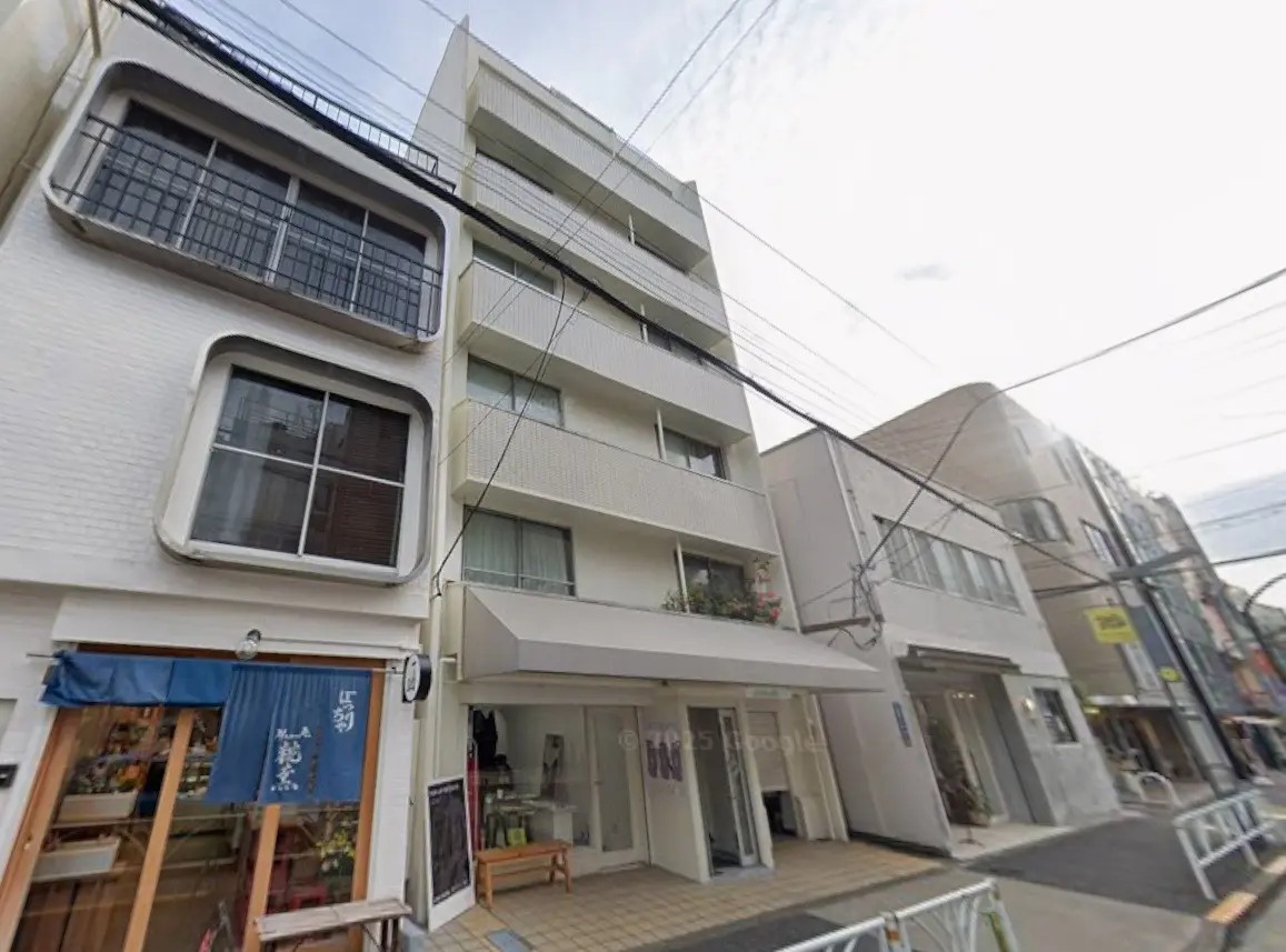 日本の住宅街にある商店とアパートが混在する建物の外観、白壁にユニークな窓デザイン