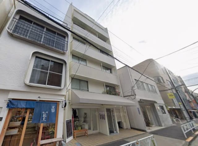 日本の住宅街にある商店とアパートが混在する建物の外観、白壁にユニークな窓デザイン