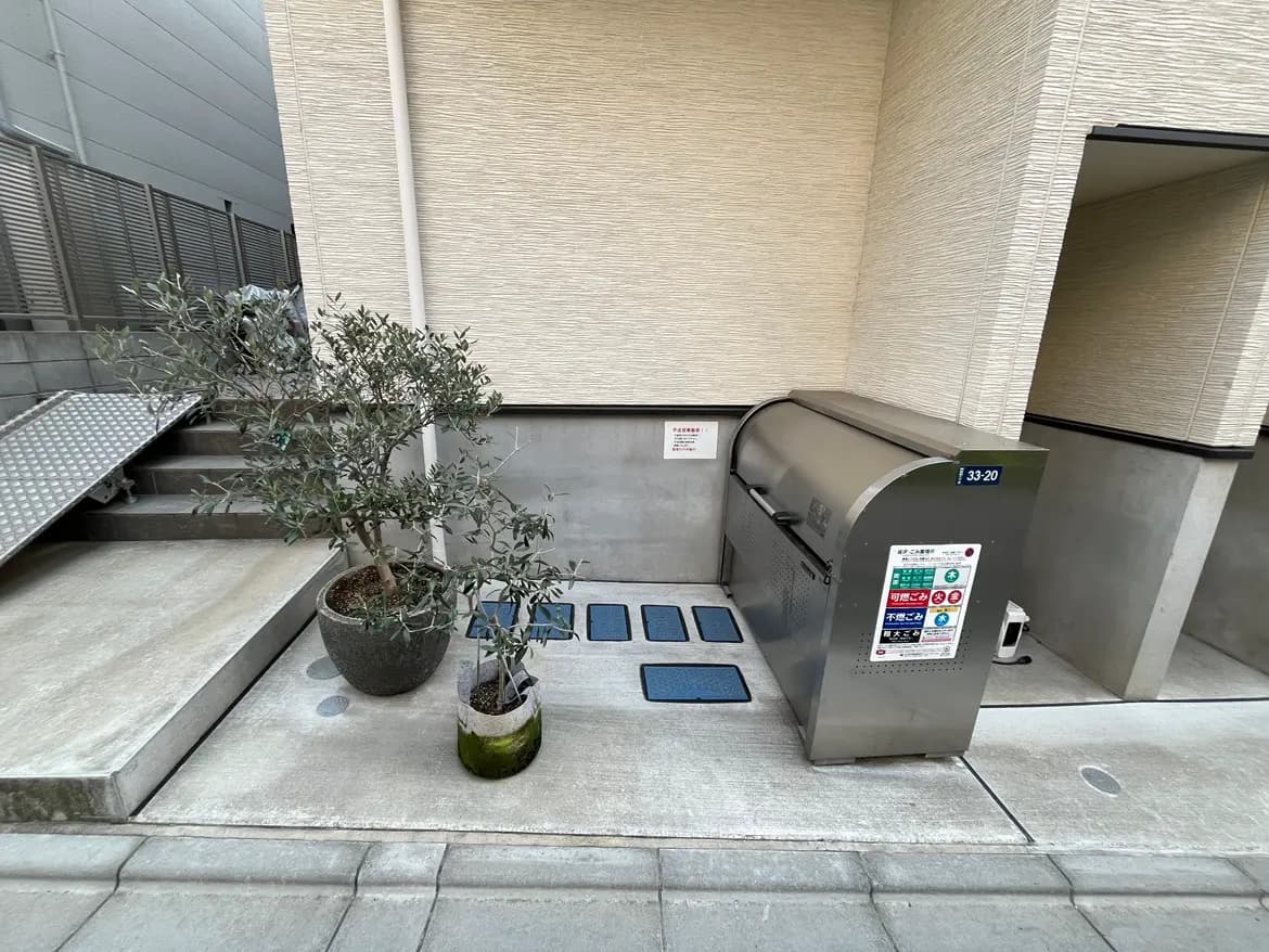 建物のエントランスに設置されたスタイリッシュなごみ収集ボックスとオリーブの木、清潔感ある都市型エクステリアデザイン