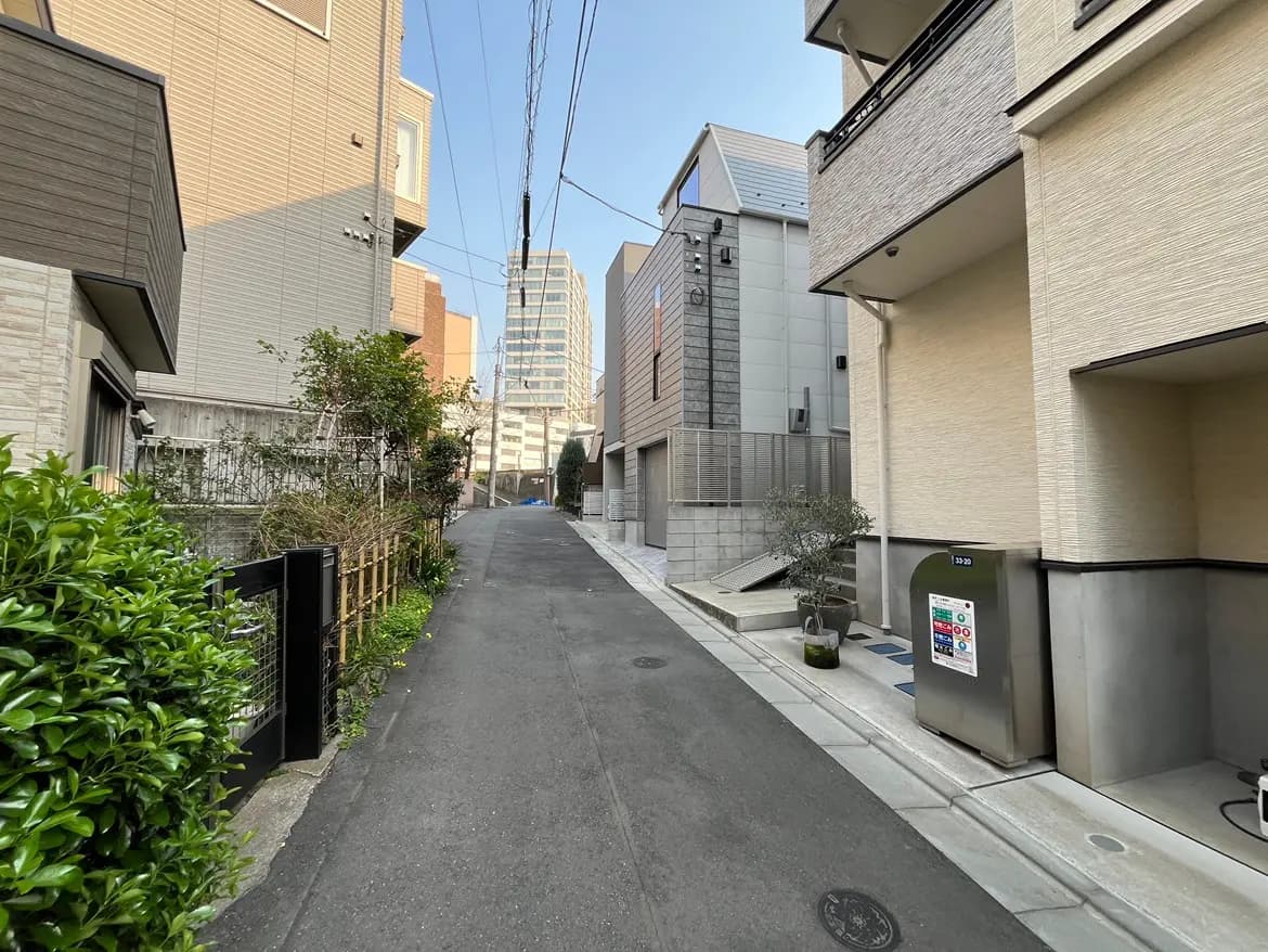 日本の都市部の狭い道、周辺の住宅と高層ビル、緑の植物とクリアな青空