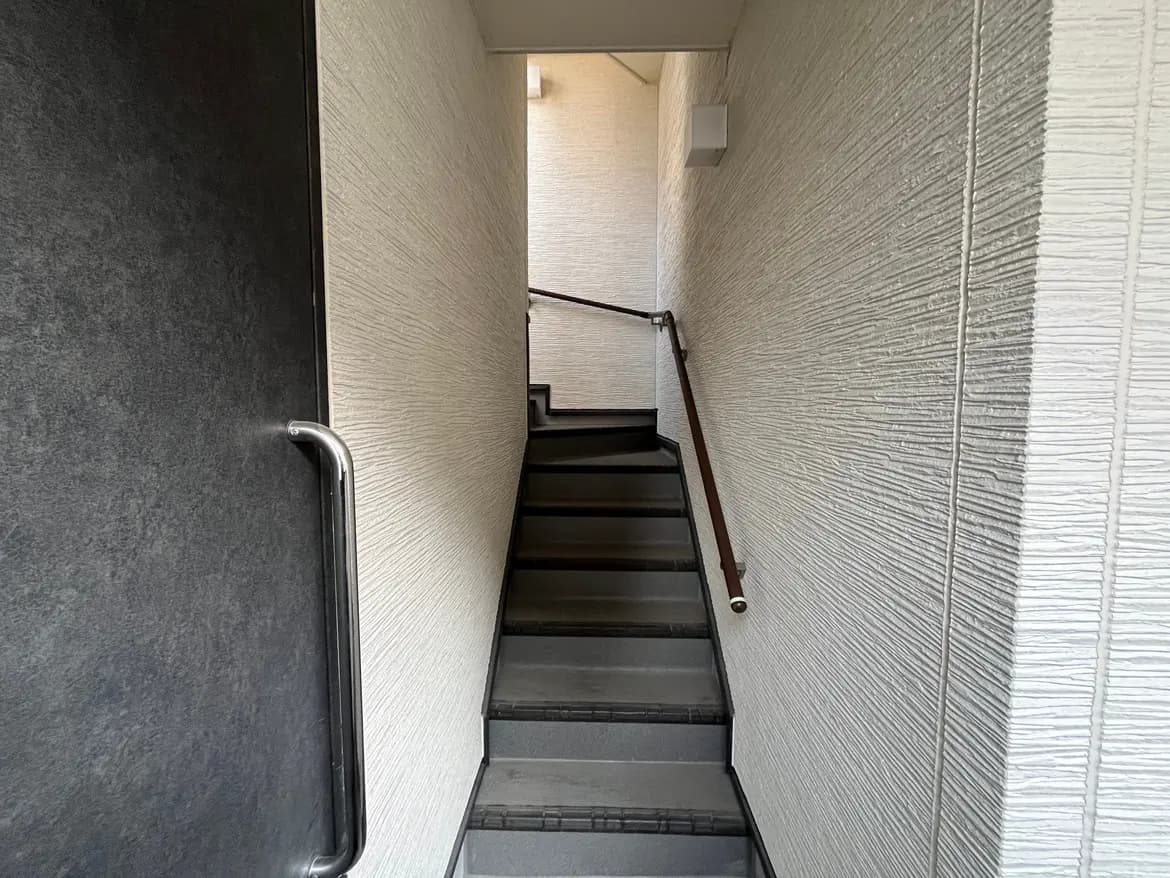 狭い空間のモノトーン階段、壁にはテクスチャーが施されており、手すりが付いている室内の写真