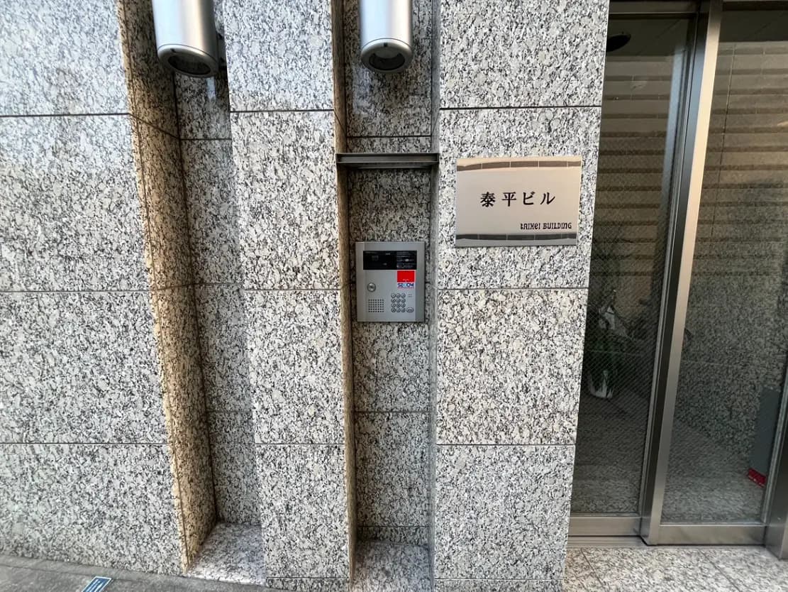 オフィスビルのエントランスに設置されたインターホンと看板、グラニット壁面とセキュリティカメラのある入り口