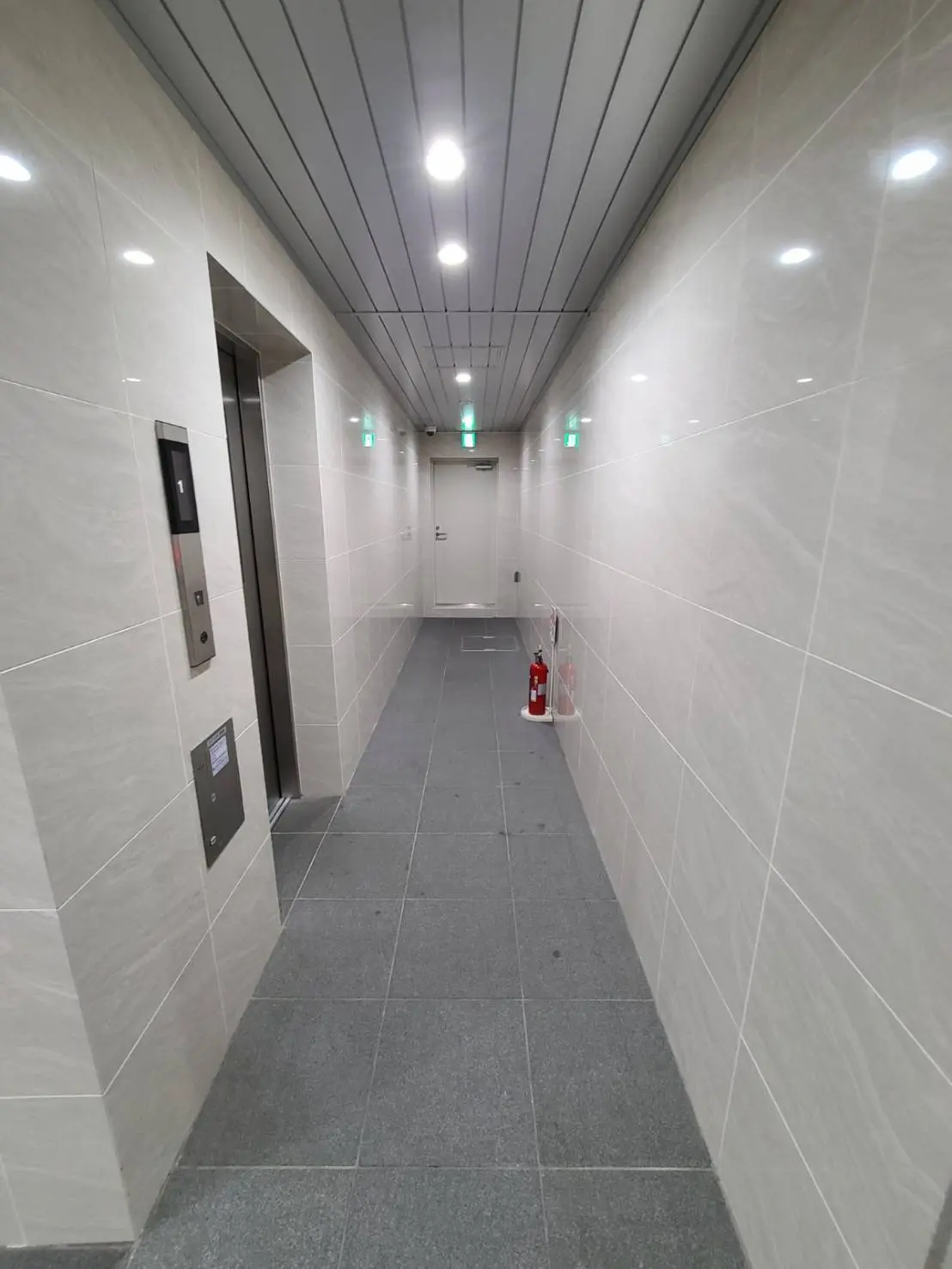 モダンで清潔なビルのエレベーターホール、白いタイルの壁、グレーの床、LED照明が明るく照らす空間