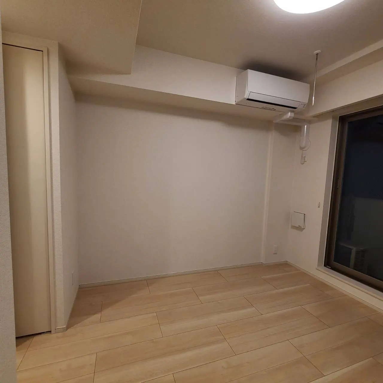 シンプルなデザインの空の部屋、木目調のタイルフローリング、壁掛け式エアコンと大きな窓のあるインテリア