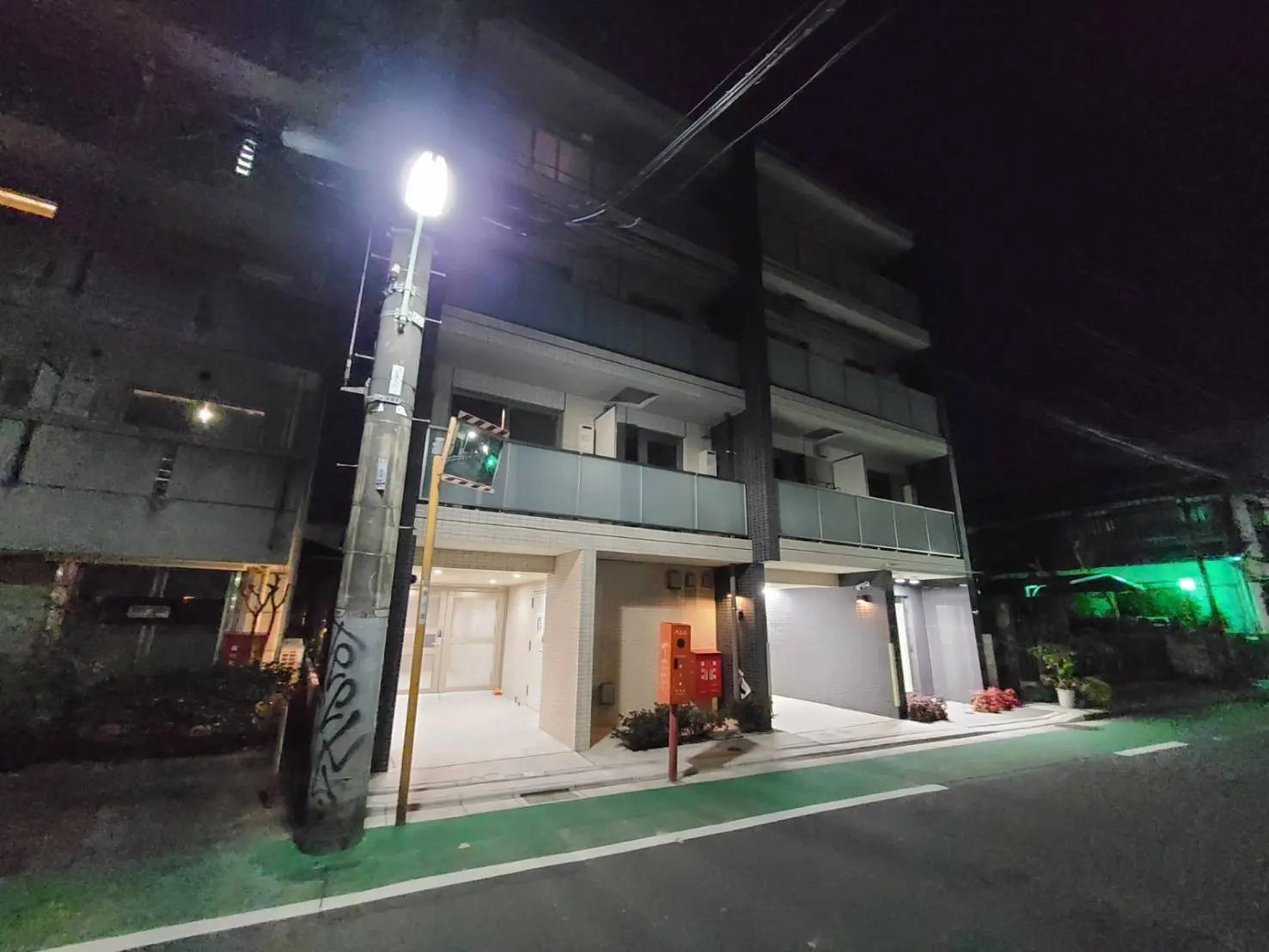 夜間の住宅街、街灯が点灯した道路沿いのマンションの外観