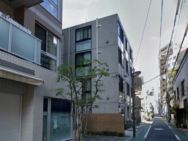 - 都市の住宅街にあるモダンなコンクリート造の建物と周辺の街並み、緑の木々が印象的な風景