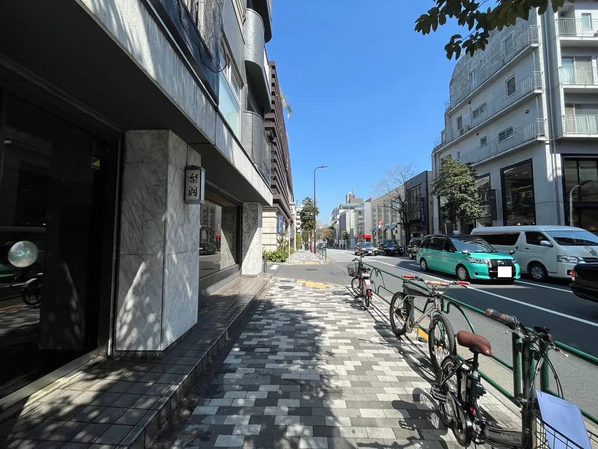 晴れた日の都市の通り、歩道と建物、駐輪された自転車と走行中の緑色のタクシー