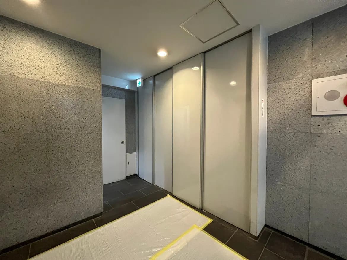 建物のエレベーター前のフロア、灰色の壁面、白いドア、バリアフリー対応のスロープがある通路