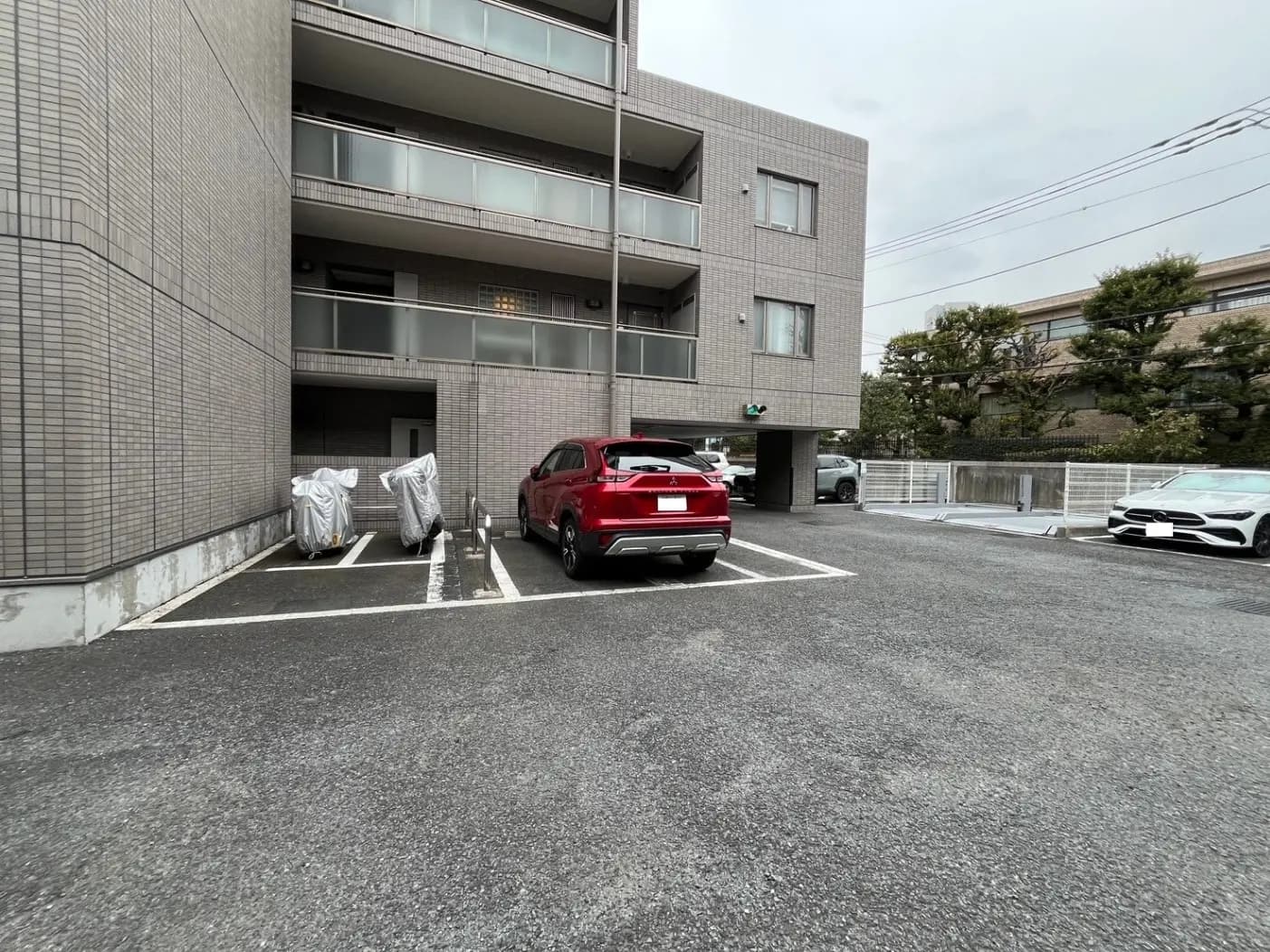 駐車場に停まっている赤いSUV車、背景には現代的なアパートの建物、アスファルトの地面