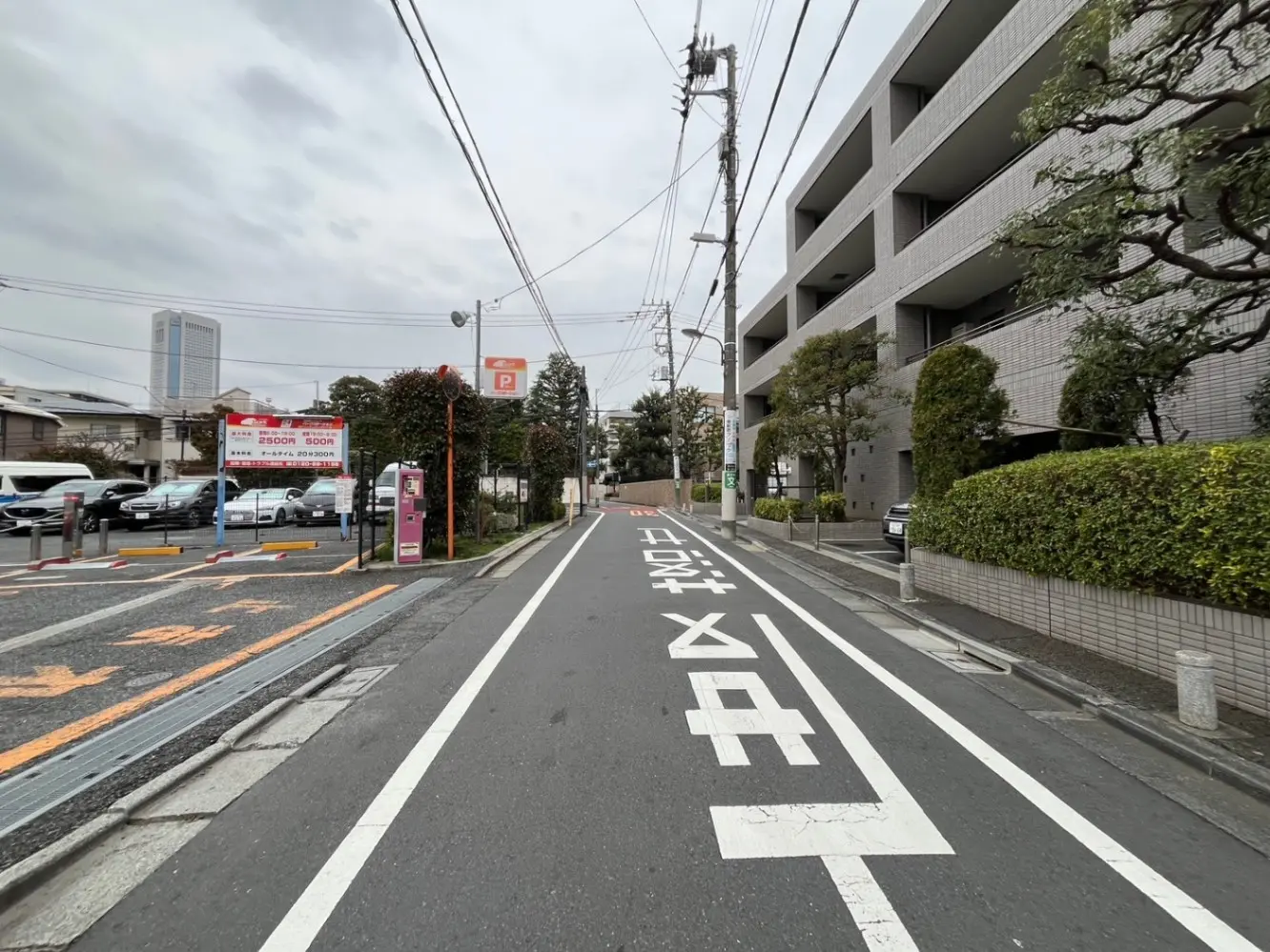 市街地の道路と駐車場の看板、曇り空の下で電柱と建物が並ぶ都市景観