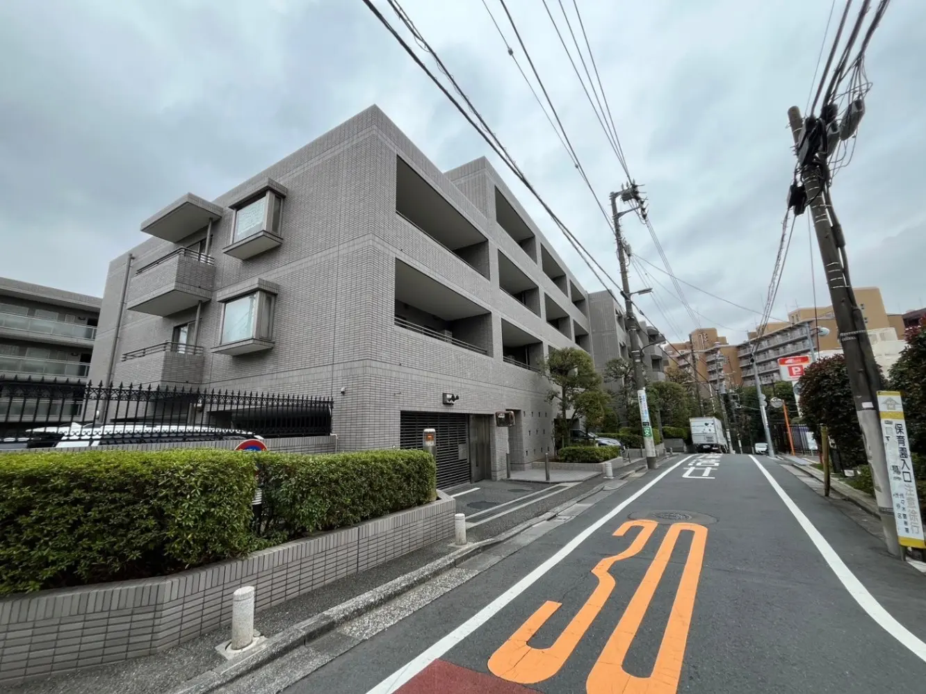 都市の通りに面したモダンな外観のマンション、道路標識あり、くもり空