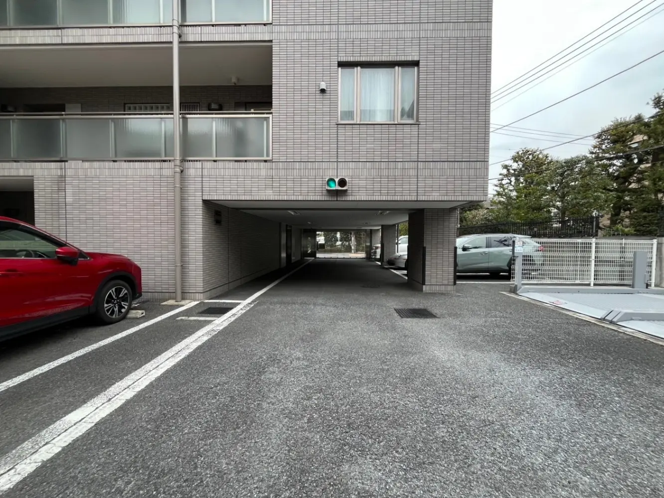 マンションの駐車場入り口、赤い車が停車中、タイル張りの外壁と柱