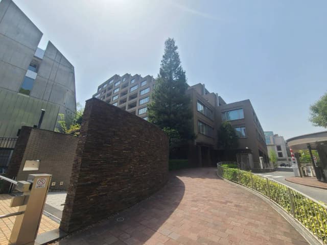 - 現代的な建物と植えられた大きな木、石造りの壁に囲まれたエントランス、晴れた青空が背景の風景