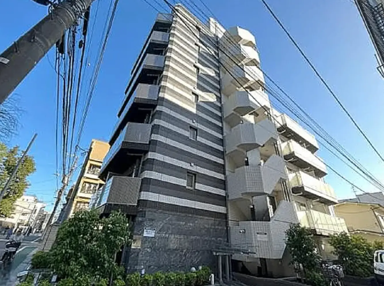 - モダンな外観の高層マンション、黒と白のストライプデザイン、周囲に緑と電柱がある都市景観