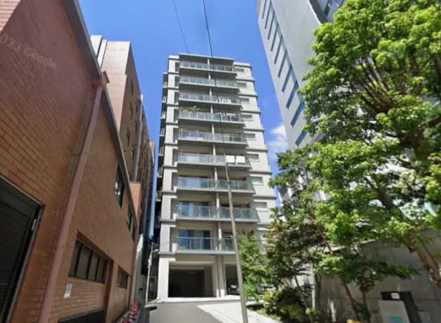都市部に位置する現代的なマンション、晴天の下、緑豊かな樹木と共に街並みを形成