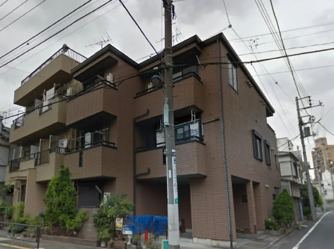 - 褐色の外壁を持つ3階建て住宅、ベランダ付きで周囲には緑が見える都市の風景