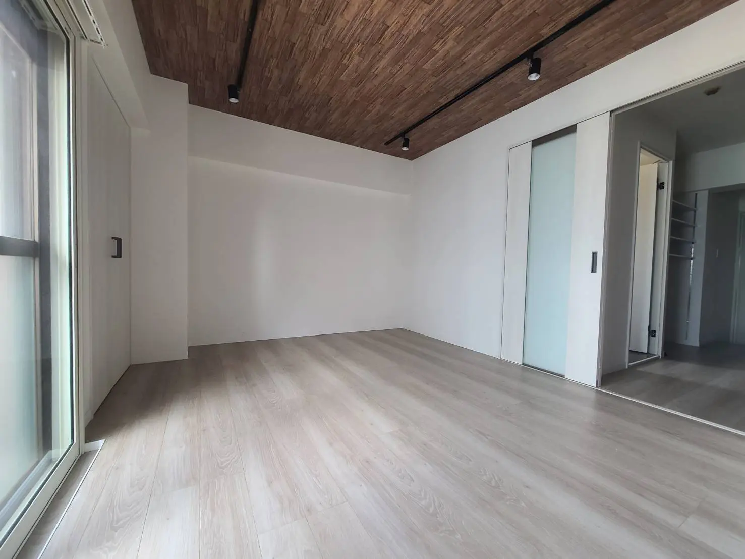 木目調フロアが特徴的なモダンな空の部屋、白い壁と木の天井、クローゼットと階段が見えるインテリア