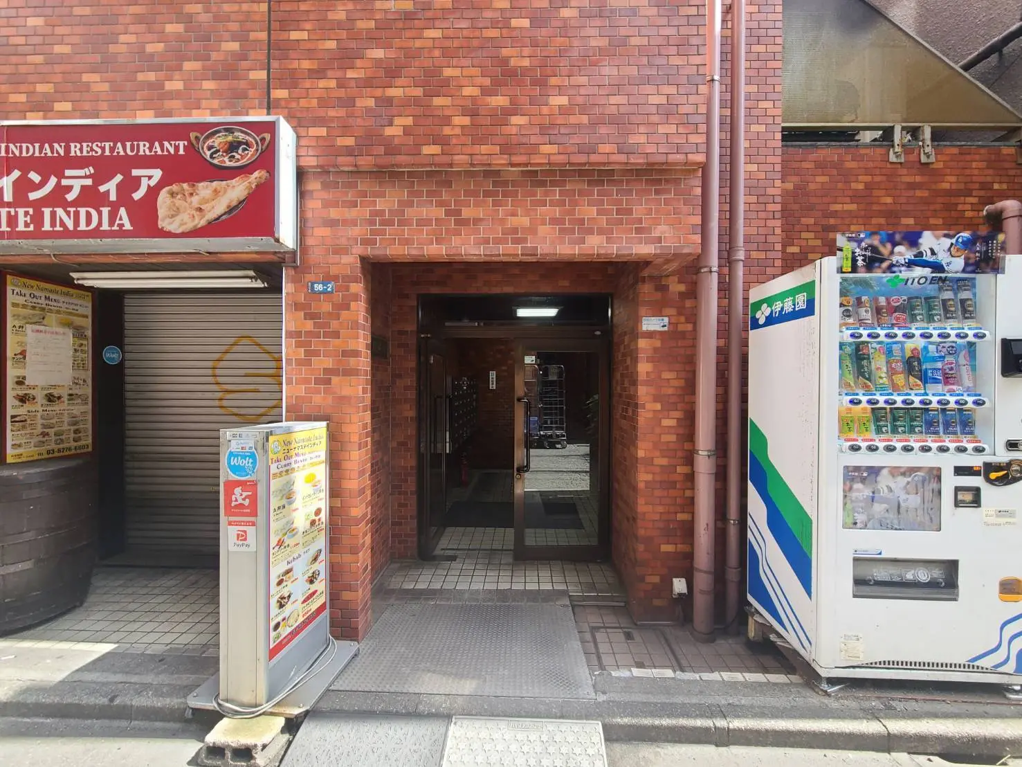 都会のレンガ壁に囲まれた通路、インド料理レストランの看板と自動販売機が見える街角