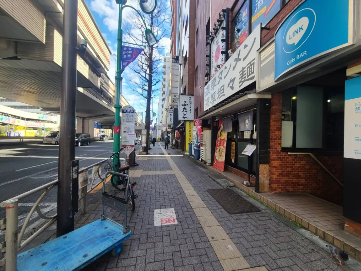 日本の都市部の歩道と商店街、快晴の日に撮影、看板や街路樹が見える風景