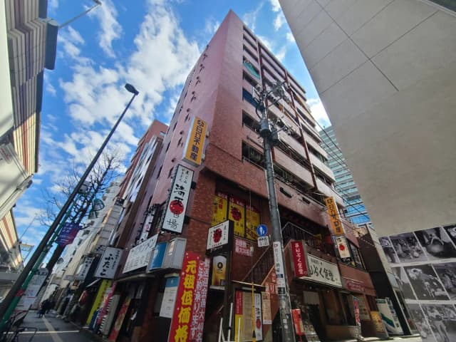 日本の都市部の狭い通りに位置する多様な看板が掲げられた飲食店が並ぶビル、晴れた日の青空
